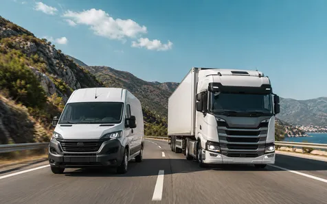 A white van and a truck driving on a coastal highway