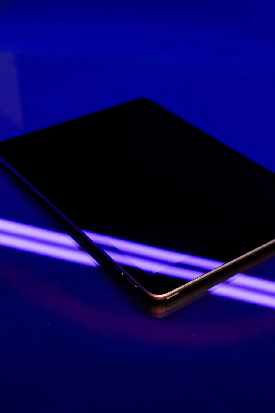 A dark tablet lying on a surface lit by violet neon light